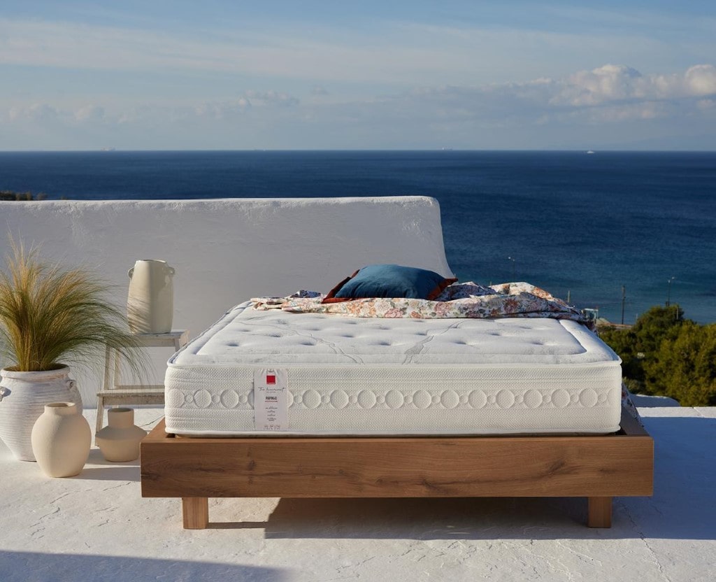 Anatomical Queen size sleeping mattress, on a wooden bed frame, lying in an outdoor area with sea view.