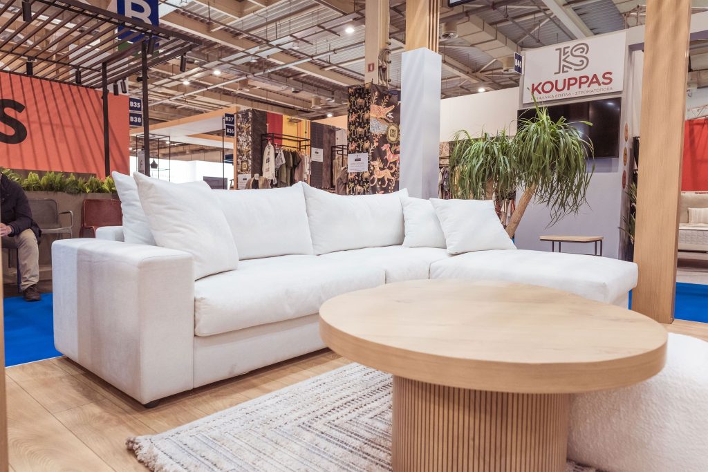 Large corner sofa in white-grey color. In front of it there is a small round brown coffee table.