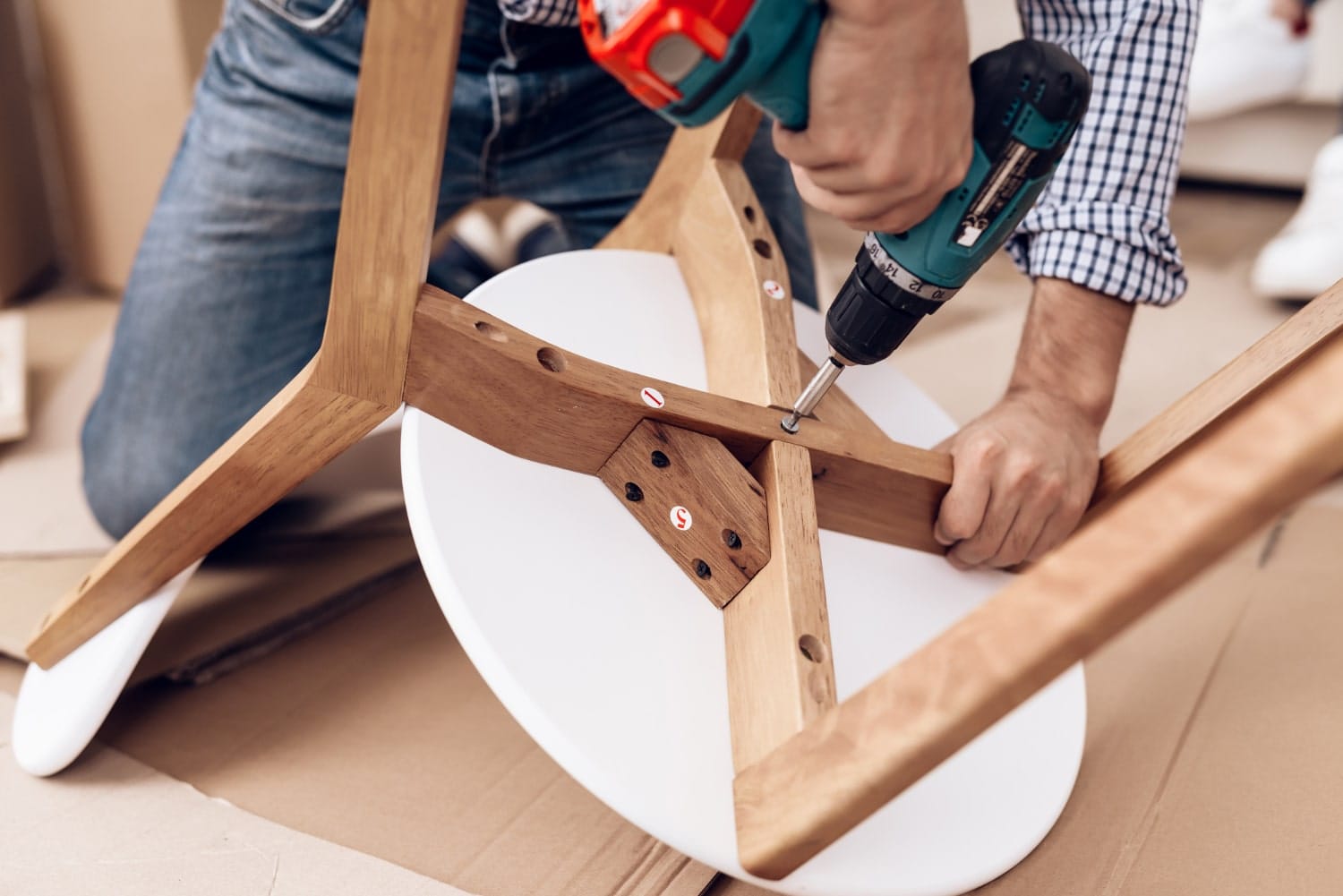 A cabinetmaker makes a handmade chair and fixes screws on it with a drill.