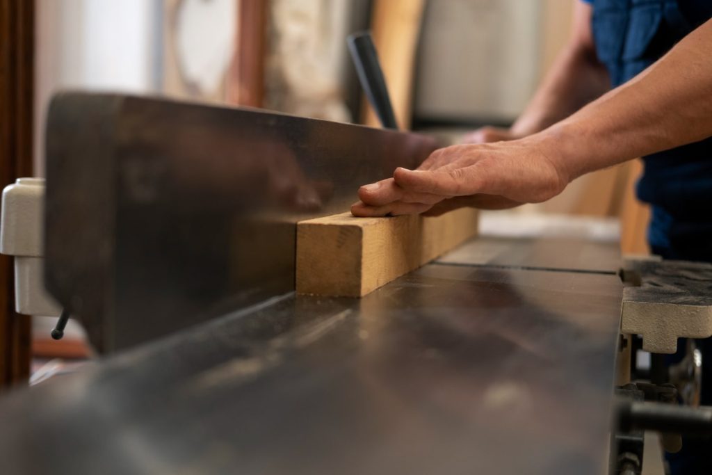Θεματική εικόνα για τα custom έπιπλα και τα οφέλη τους. Επιπλοποιός κόβει μια ξύλινη σανίδα για την κατασκευή ενός επίπλου.
