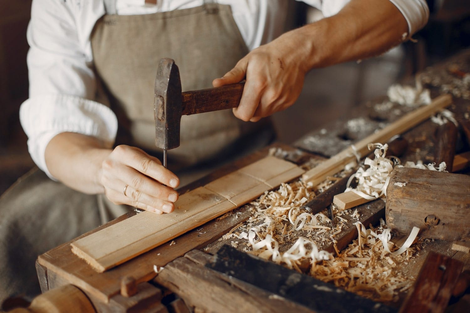 A specialist craftsman makes custom-made furniture using a hammer and driving a nail.